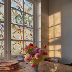 a vase filled with flowers sitting on top of a wooden table next to two windows