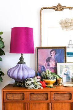 a purple lamp sitting on top of a wooden dresser next to a mirror and potted plant