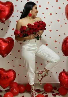 a woman in white pants and heels holding red roses next to balloons with hearts on them