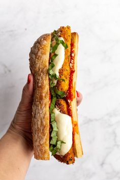 a hand holding a sandwich with meat, cheese and lettuce on it in front of a marble background