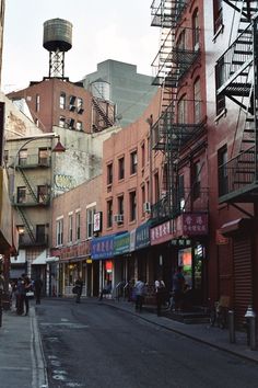 people are walking down the street in front of buildings with fire escapes on each side