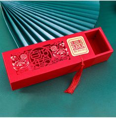 an open red box with chinese writing on the lid and tassels attached to it