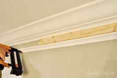 a person using a power drill to fix a beam in a room with white walls