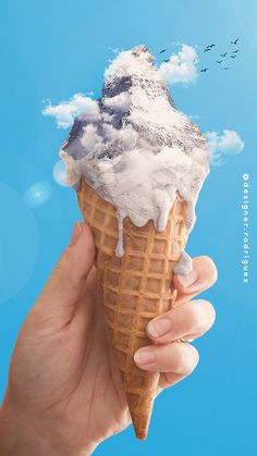 a hand holding an ice cream cone in front of a blue sky with birds flying around