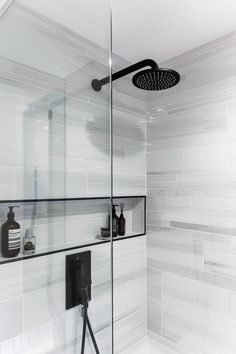 a shower with glass walls and white tile in the shower area is shown here, there are black accessories on the shelf next to the shower head