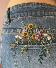 a woman's jeans with flowers embroidered on the side and back pocket, in front of her belly