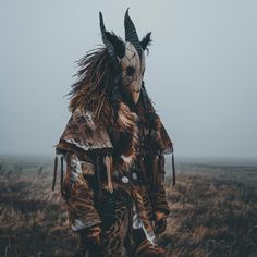 a person with horns and makeup standing in a field on a foggy, cloudy day