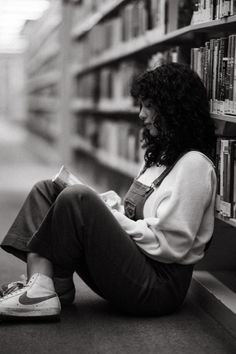 A black and white photograph of a woman sitting on the ground of a library reading a book. Photography Poses In Library, Cute Library Pictures, Photography In Library, Photoshoot In A Library, Photoshoot Moodboard Inspiration, Photoshoot Library Photo Ideas, Photoshoot In Bookstore, Ny Public Library Photoshoot, Nerdy Photoshoot Ideas