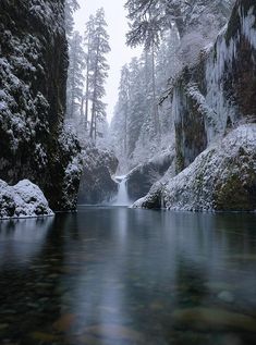 a river surrounded by snow covered rocks and trees in the distance with water running through it