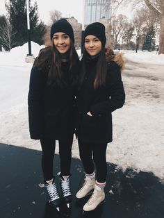 two young women standing next to each other on a snow covered ground with buildings in the background