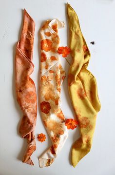 three scarves laying on top of each other in different colors and patterns, one with an orange flower