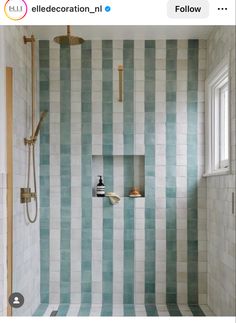 a bathroom with blue and white striped tile on the walls, shower head, and window