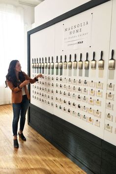 a woman standing in front of a large display of perfume bottles on a wall next to a window