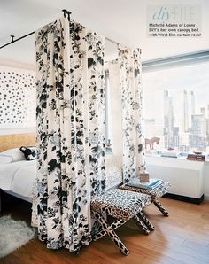 curtain rods attached to the ceiling form a canopy bed with black and white flowers on it