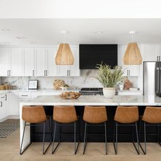 a kitchen with white cabinets and marble counter tops, black appliances and pendant lights hanging from the ceiling