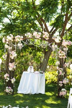 an outdoor wedding setup with white linens and pink flowers on the table, surrounded by greenery