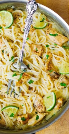 a skillet filled with chicken, noodles and limes on top of a wooden table