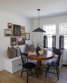 a dining room table with two chairs and a bench in front of the window that has pictures on the wall above it