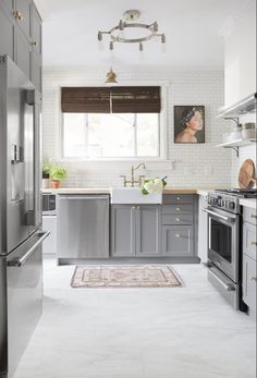 a kitchen with stainless steel appliances and white tile flooring that has an area rug on the floor