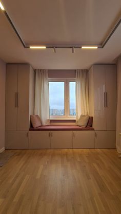 an empty room with a window seat and some curtains on the windowsill, in front of a city view