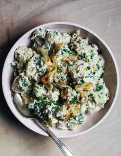 a white bowl filled with food on top of a wooden table next to a spoon