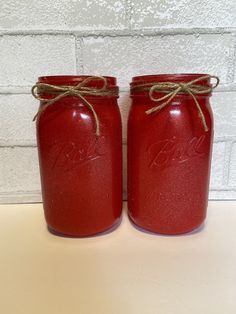 two red mason jars tied with twine and sitting on a table next to a brick wall