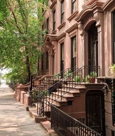 a row of brownstone townhouses with wrought iron railings and trees on the sidewalk