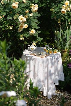 a table in the middle of a garden with flowers around it and a tea pot on top