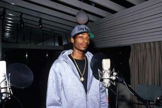 a young man standing in front of a microphone wearing a hoodie and holding a baseball cap