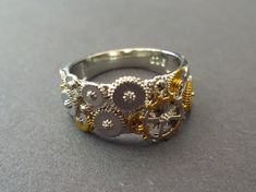 This listing is for a unique Iron Alloy Metal Gear ring. The steampunk style ring features a mix of silver and gold color machinery gears. This detailed ring is perfect for a steampunk or gothic punk style. Type- Ring Sub-Type- Metal Ring  Style- Punk, Gothic, Steampunk  Size/Length- US/Canada Sizing; Sizes 6-12 Accents- Mixed gears Metal Type- Iron Alloy Metal  Why should you shop with Beadology By Heather? -We have a large amount of premium beads and supplies that we offer with your budget in Gear Ring, Steampunk Rings, Gothic Steampunk, Steampunk Style, Punk Bands, Detailed Ring, Gothic Punk, Style Punk, Special Jewelry