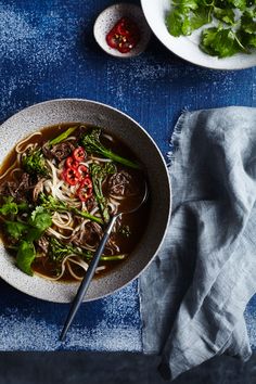 a bowl of beef and noodle soup with chopsticks on a blue cloth