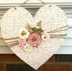 a heart shaped sign with flowers hanging from it's side on a brick wall