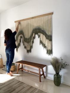 a woman hanging curtains on the wall in her living room with a wooden bench and table