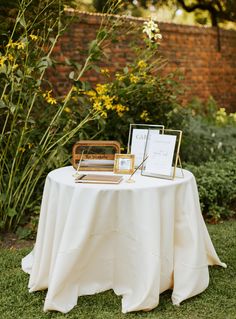 the table is set up for an outdoor ceremony with pictures on it and flowers in the background