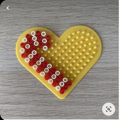 a yellow and red heart shaped beaded object on a wooden table with white dots