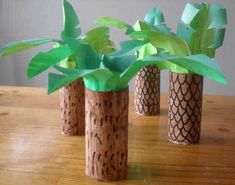 three vases with plants in them sitting on a wooden table together, one is made out of cardboard and the other has green leaves