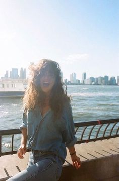 a woman sitting on the edge of a pier next to the ocean with a city in the background