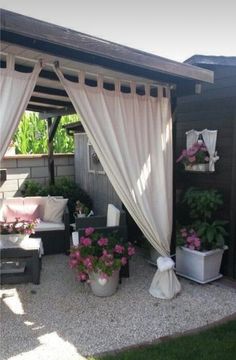 an outdoor living area with white curtains and pink flowers