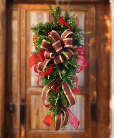 a christmas wreath hanging on a door with red and green ribbons, evergreens and poinsettia