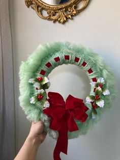 a hand holding a wreath with red and white flowers on it next to a mirror