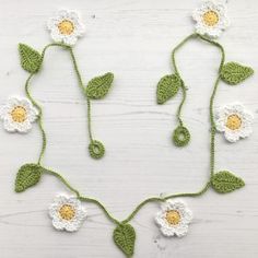 a crocheted necklace with white flowers and green leaves