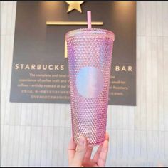 a person holding up a pink drink in front of a starbuck's sign