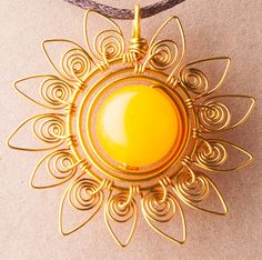 a gold pendant with an orange stone in the center on a gray cord necklace that is attached to a leather cord