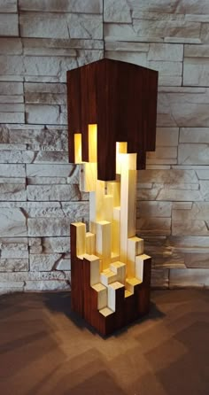 a sculpture made out of wooden blocks with lights on it's sides and in front of a brick wall