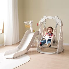 a toddler sitting in a swing with a basketball hoop on the wall behind it