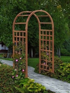 an arch made out of wood with pink flowers growing on it in the middle of a garden