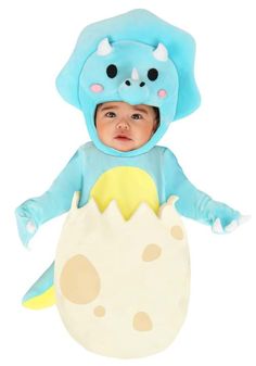 a baby in a blue dinosaur costume is sitting on top of an easter egg with its arms out