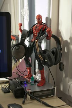 a spider - man figure with headphones on stands in front of a computer