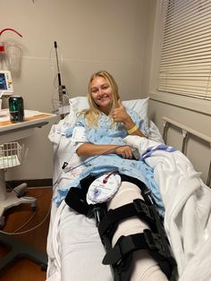 a woman laying in a hospital bed giving the thumbs up