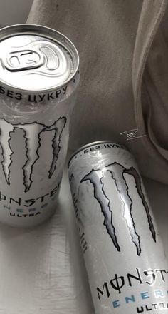 two cans of energy drink sitting on top of a white table next to a bag